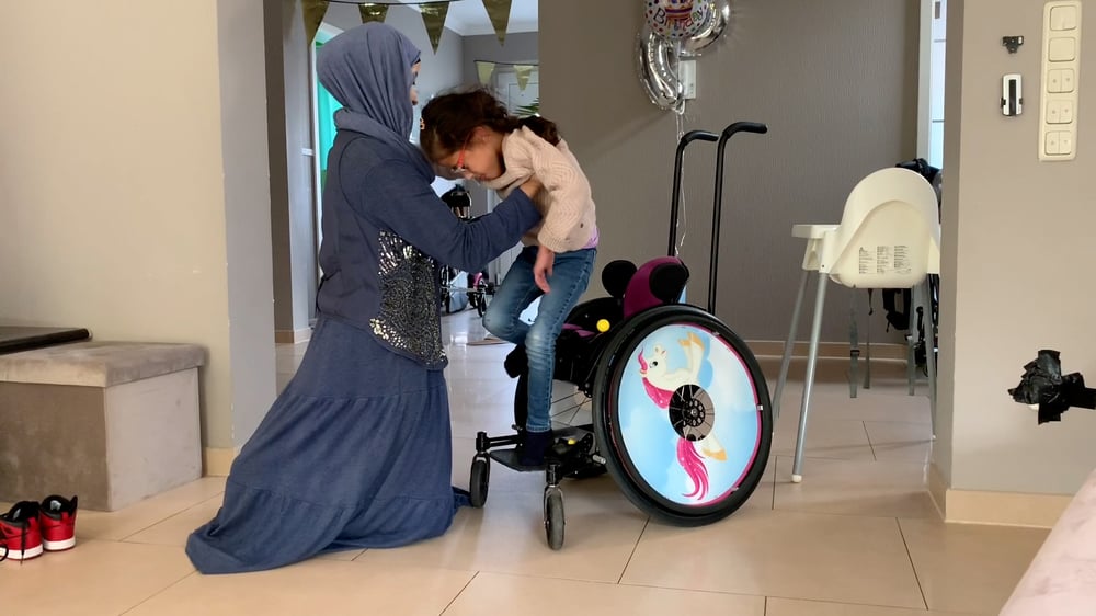 Mamma lyfter sitt barn i rullstol