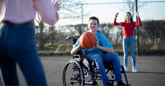 Tonårspojke i rullstol spelar basket med vänner.