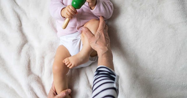 Liten bebis som får osteopatisk behandling av sitt ben för att förhindra höftledsdysplasi av barnsjukgymnast.