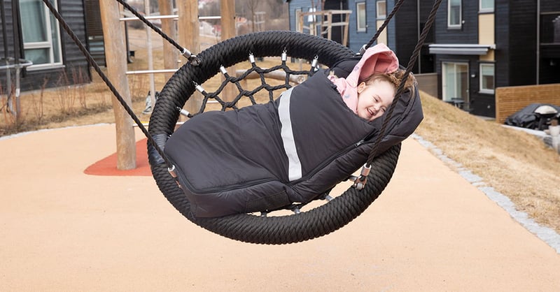Young girl is wrapped in a heating bag while swinging on the swing and laughing.