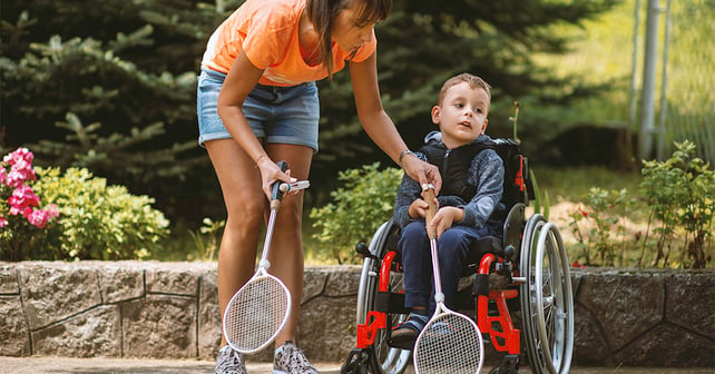 Disabled boy sitting in wheelchair and playing badminton with his mother