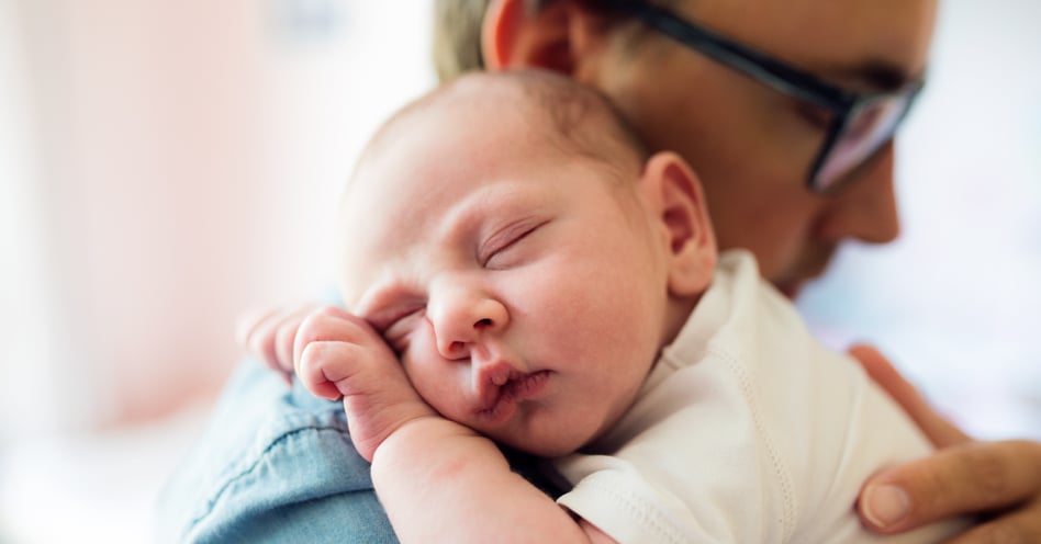 infant lies sleeping on his father's shoulder