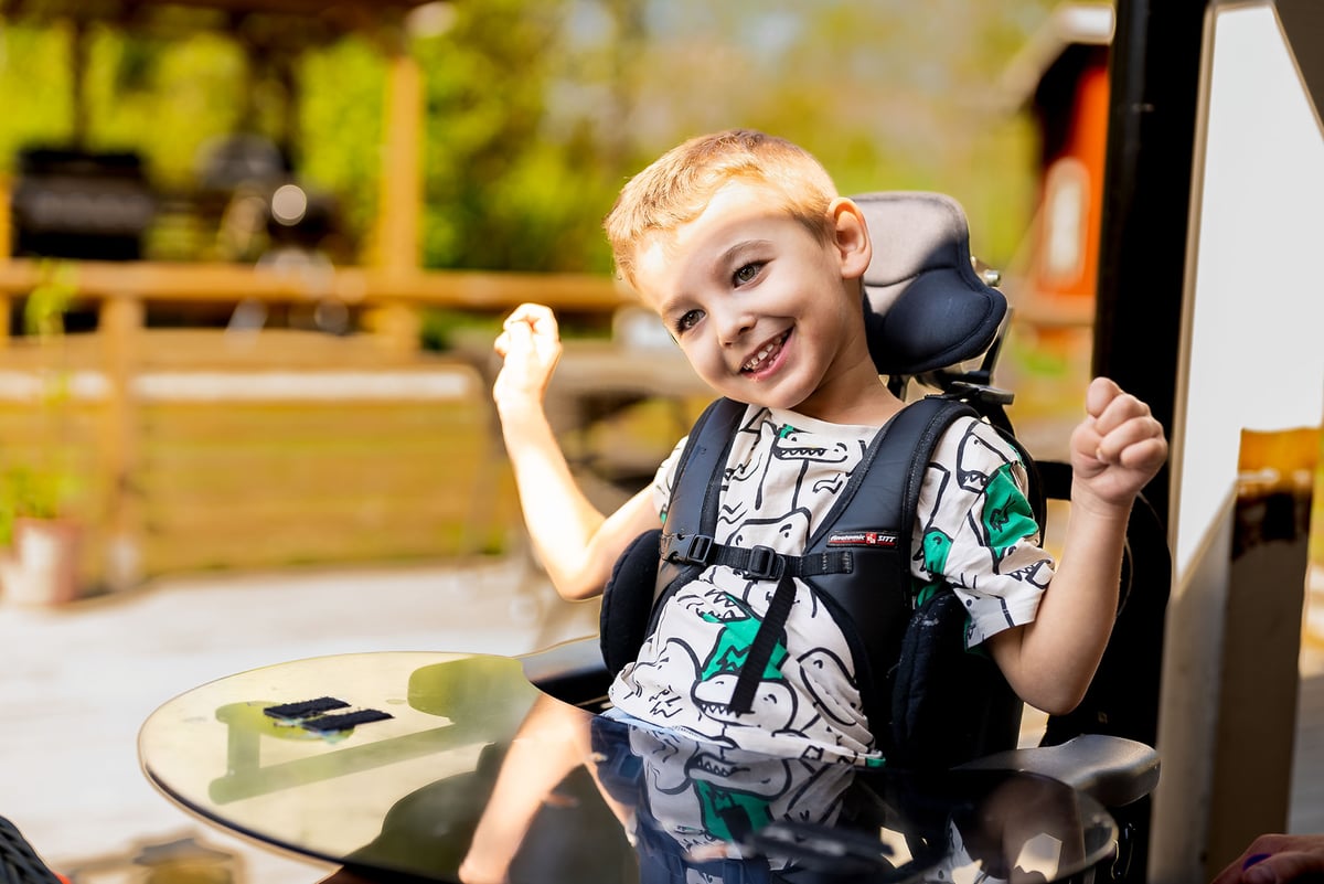 Young boy with CP smiles while sitting in a wheelchair.