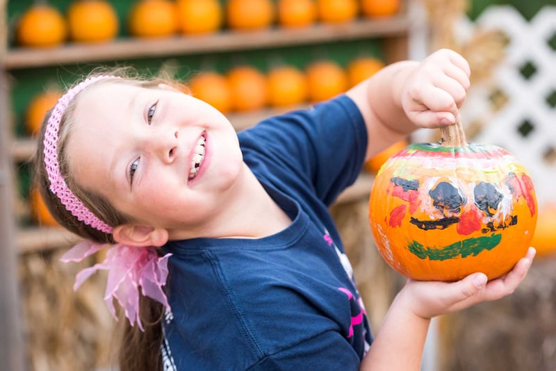 Smiling little girl showing her painted pumpkin
